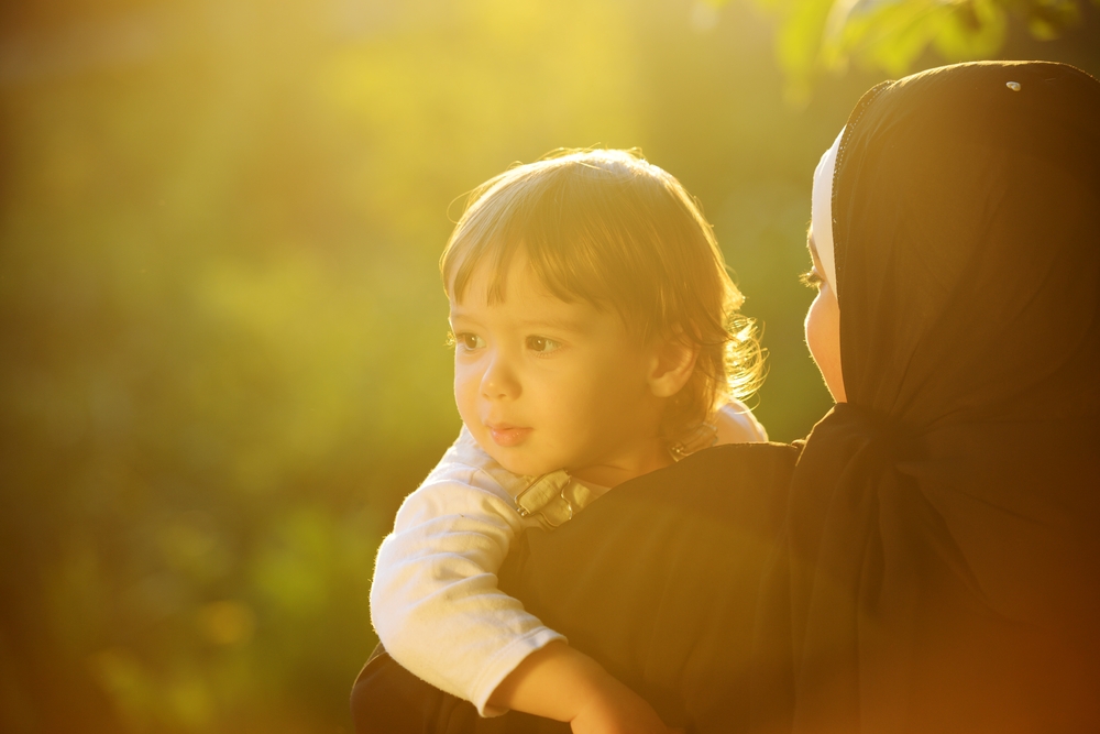 Middle Eastern Muslim mother playing with her little baby in green park and holding him in arms Middle Eastern Muslim mother playing with her little baby in green park and holding him in arms